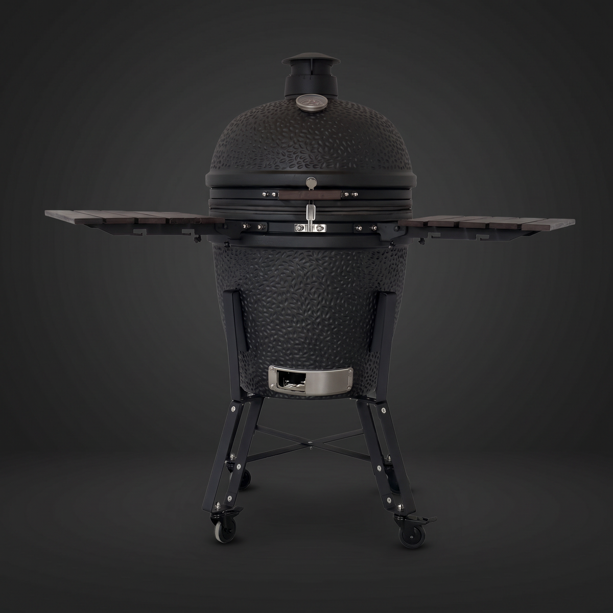 Zwarte Vuur kamado 22 inch, gesloten, rechte voorkant, met de twee roodbruine houten zijtafels uitgeklapt, op een donkere achtergrond.
