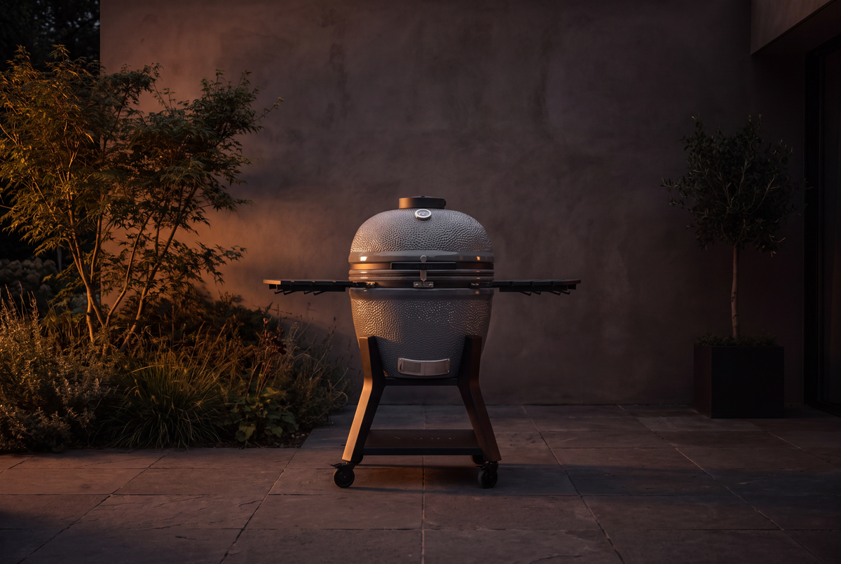Een grote, gesloten keramische kamado op een schemerig terras, geen personen in beeld.