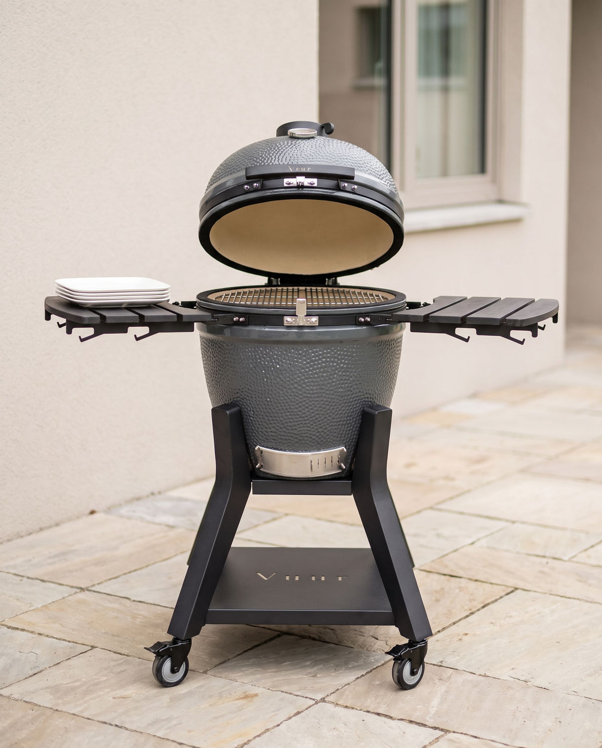 Kamado met open deksel en een stapel borden als schaalreferentie, geen personen.