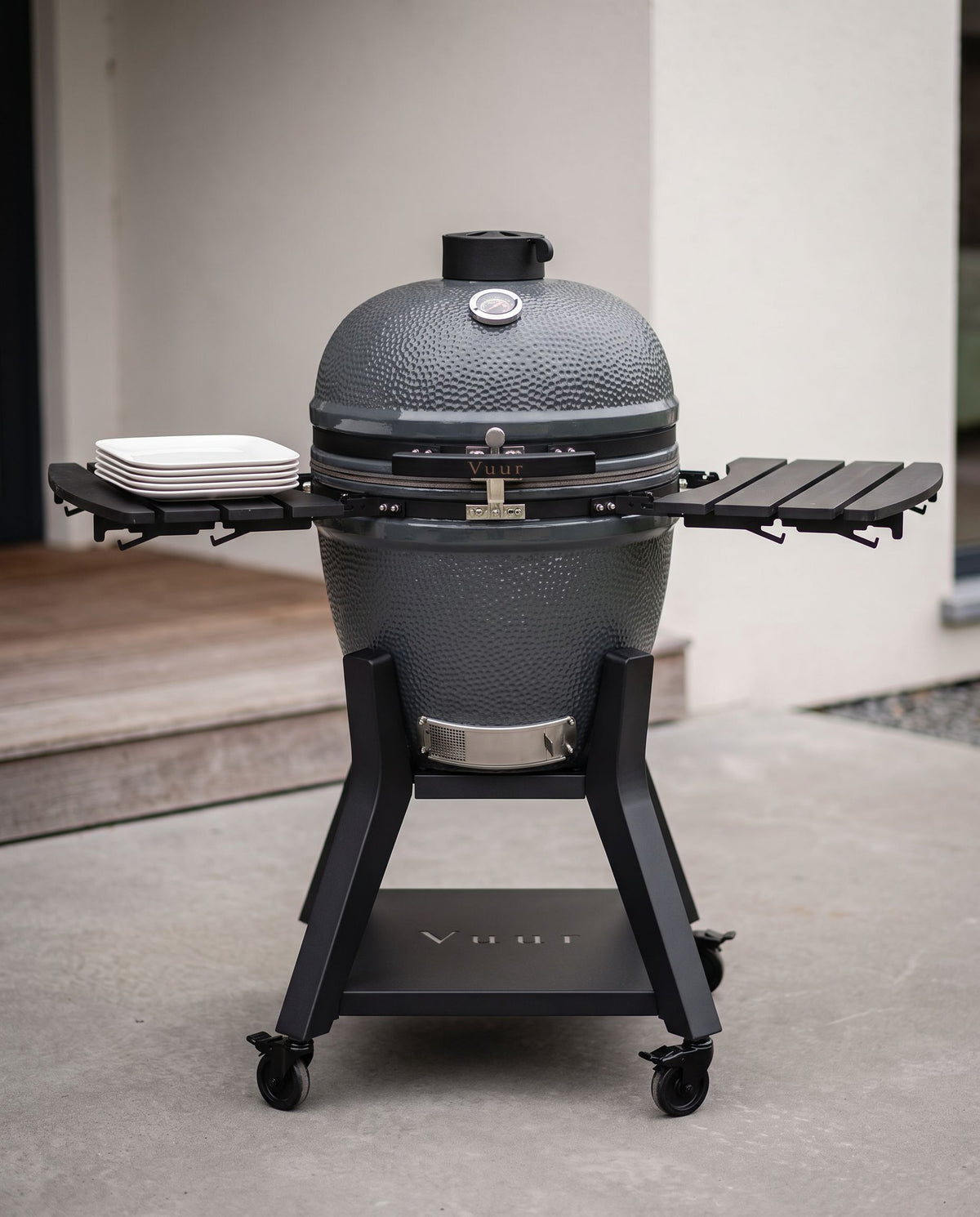 Kamado met open deksel en een stapel borden als schaalreferentie, geen personen.