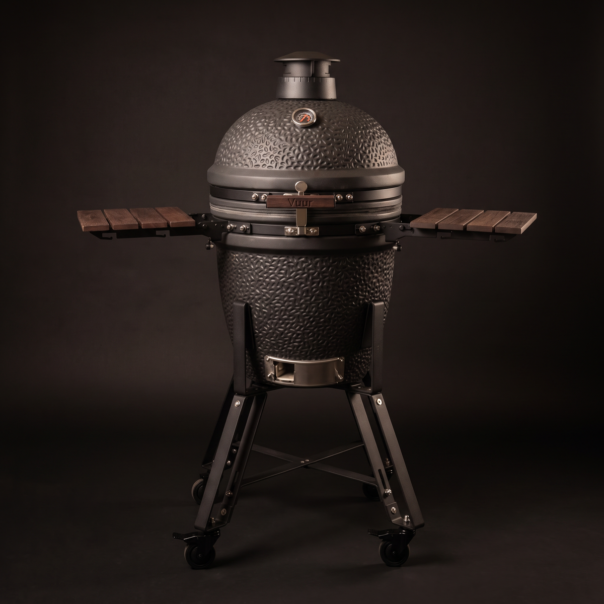 Zwarte Vuur kamado 18 inch, gesloten, rechte voorkant, met de twee bamboe zijtafels uitgeklapt en de naam Vuur op het handvat, op een donkere achtergrond.